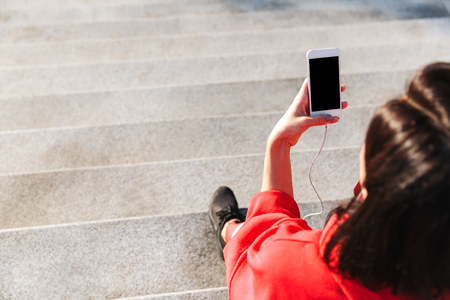 Top view of a young sportswoman holding mobile phone, listening to music with earphones, drinking waterの写真素材