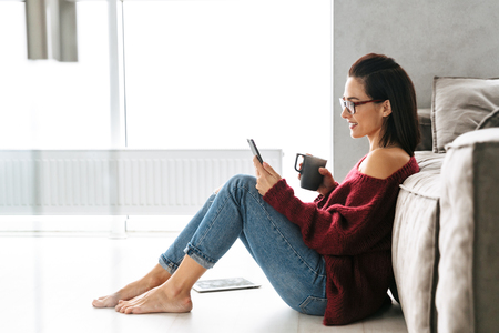 Image of a beautiful woman indoors in home on sofa using mobile phone.の写真素材