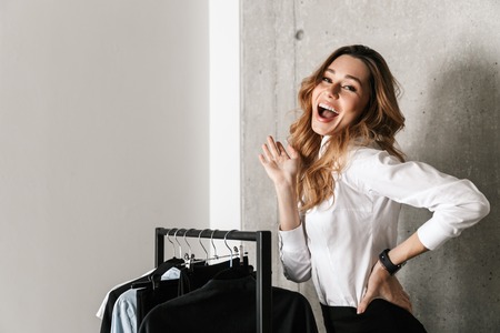 Photo of beautiful young business woman dressed in formal clothes shirt indoors standing near hanger.の写真素材