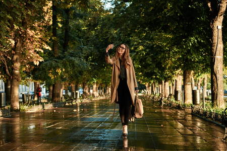 Portrait of joyous woman 20s wearing coat and eyeglasses using cell phone while walking through empty alleyの写真素材