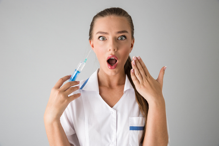 Photo of a beautiful young woman cosmetologist doctor isolated over grey wall background holding injection syringe.の写真素材