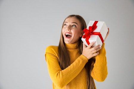 Image of a beautiful shocked happy young woman isolated over grey wall background holding gift present box.の写真素材