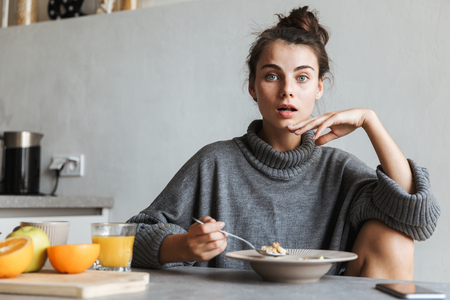Beautiful young woman having healthy breakfast while sitting on a kitchenの写真素材