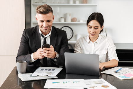 Image of a happy handsome business man work indoors with his colleague woman using laptop computer and mobile phone.の写真素材