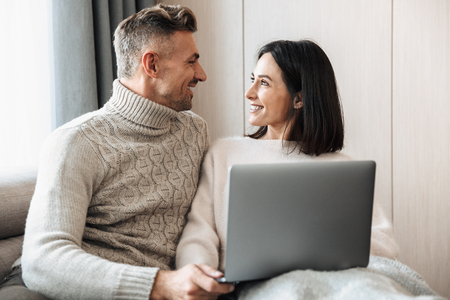 Image of a happy loving couple family sitting on sofa indoors on sofa using laptop computer.の写真素材