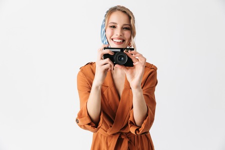 Portrait of a beautiful young blonde pretty woman wearing silk scarf posing isolated over white wall background holding camera photographing.の写真素材