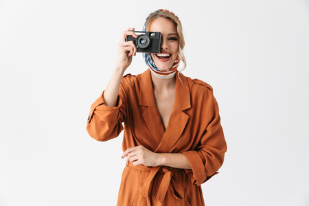 Portrait of a beautiful young blonde pretty woman wearing silk scarf posing isolated over white wall background holding camera photographing.の写真素材