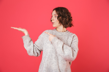 Portrait of a cheerful young woman standing isolated over pink background, presenting copy spaceの写真素材