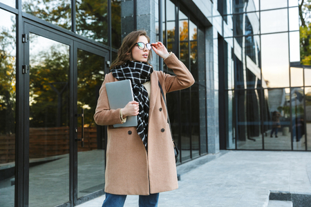 Image of a beautiful young woman outdoors walking by street holding laptop computer.の写真素材