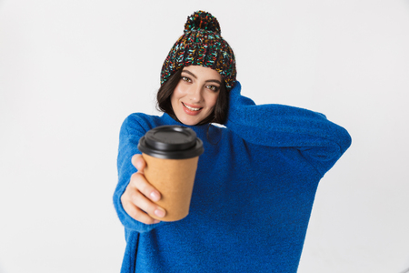 Portrait of cheerful woman 30s wearing winter hat smiling and drinking takeaway coffee while standing isolated over white backgroundの写真素材