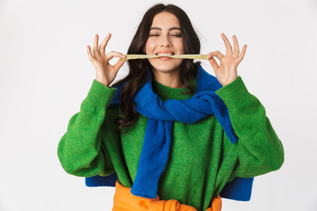 Portrait of positive woman 30s in colorful clothes chewing long gum while standing isolated over white backgroundの写真素材