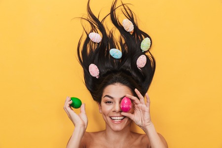 Image of beautiful pleased happy young woman lies isolated on yellow background over easter eggs covering eyes.の写真素材