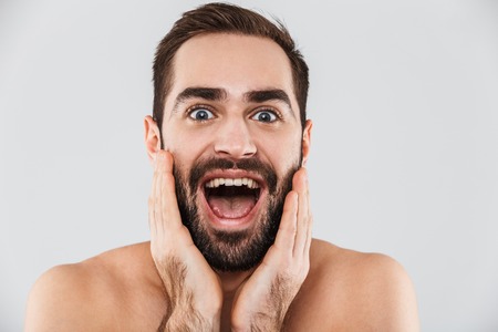 Close up of a young excited handsome bearded shirtless man standing isolated over white backgroundの写真素材