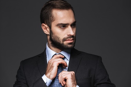 Close up of a handsome young business man wearing suit standing isolated over black background, looking awayの写真素材