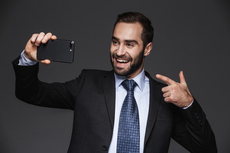 Portrait of a confident handsome businessman wearing suit isolated over black background, taking a...