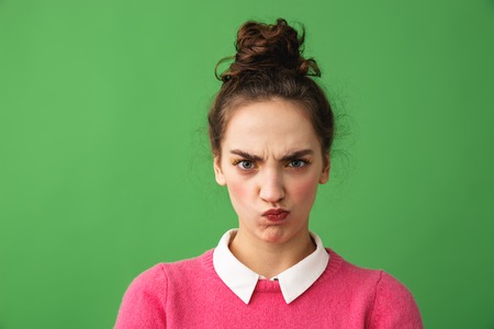 Portrait of an upset young woman standing isolated over green background