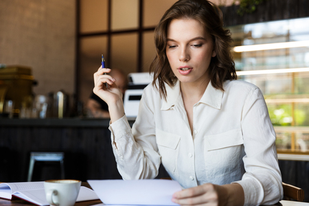 Confident businesswoman working with documents while sitting at the cafe, drinking coffeeの写真素材