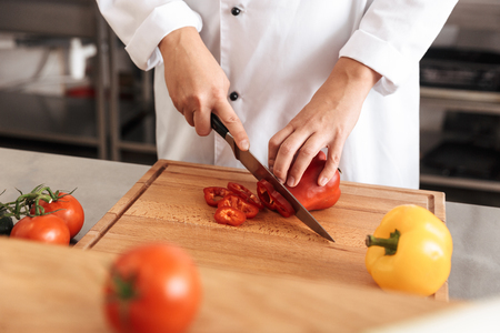 Photo of european woman chef wearing white uniform making salad with fresh tomatoes in kitchen at the restaurantの写真素材
