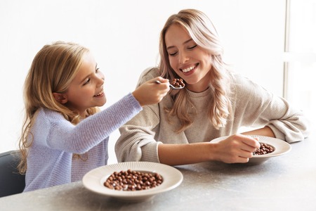 Image of two happy girls sisters at kitchen indoors eat have a breakfast together.の写真素材