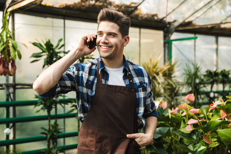 Image of gardener man posing in the nature greenhouse garden talking by mobile phone.の写真素材