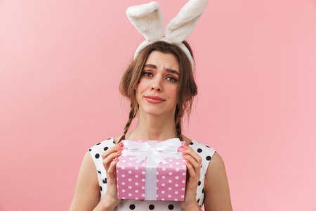 Portrait of a pretty lovely girl wearing bunny ears standing isolated over pink background, holding gift boxの写真素材