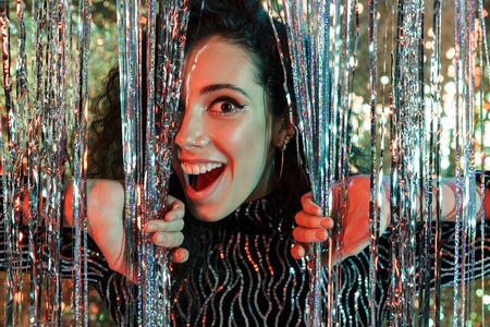 Portrait of a cheerful beautiful woman wearing bright clothes and makeup standing over sparkling background, posingの写真素材
