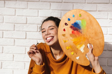 Lovely artistic woman holding color palette for painting indoors over white wallの写真素材