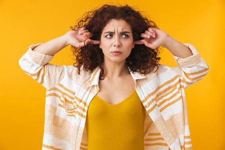Image of a displeased beautiful young curly girl posing isolated over yellow wall background covering ears.の写真素材