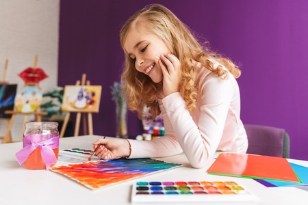 Lovely little girl painting a picture at the table at homeの写真素材
