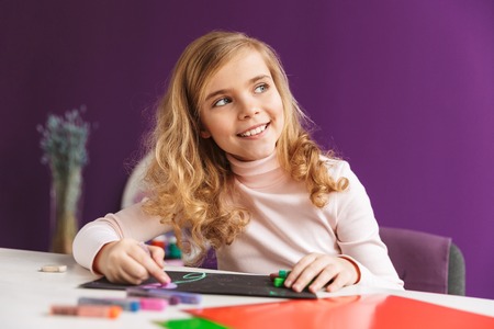 Cheerful little girl drawing a picture at the table at home