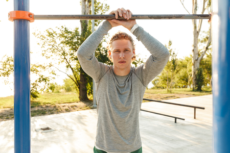 Confident young sportsman doing exercices at the horizontal bar outdoors