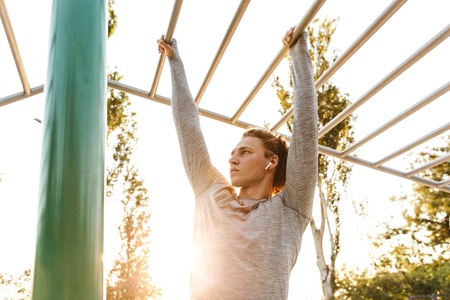 Concentrated young sportsman doing exercises on bars outdoors
