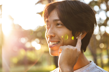 Close up of a smiling young asian man athlete listening to music with earphones at the parkの写真素材