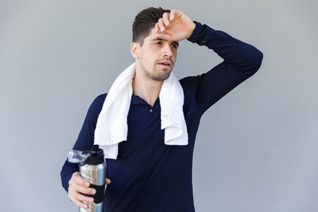 Tired sportsman holding water bottle while standing isolated over gray backgroundの写真素材