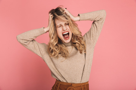 Portrait of disappointed woman 30s with blond hair grabbing her head and screaming in confusion or...
