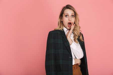 Portrait of excited woman 30s in trendy jacket wondering while posing on camera isolated over pink backgroundの写真素材