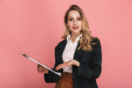 Photo of young businesswoman wearing jacket holding clipboard with chart isolated over pink backgroundの写真素材