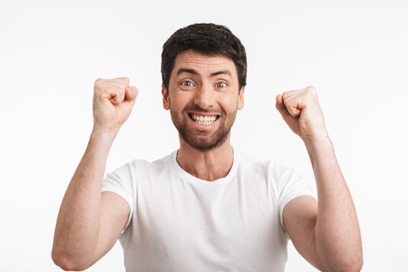 Image of ecstatic man 30s with bristle in casual t-shirt rejoicing and clenching fists isolated over white backgroundの写真素材