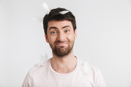 Image of happy man 30s with bristle in casual t-shirt standing under falling feathers isolated over white backgroundの写真素材