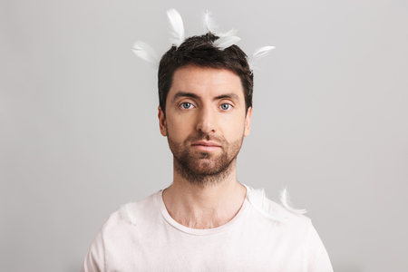 Image of handsome man 30s with bristle in casual t-shirt standing under falling feathers isolated over white backgroundの写真素材