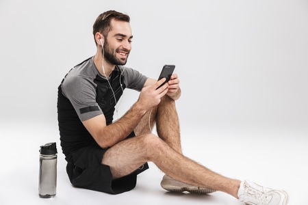 Image of a handsome young sports fitness man posing isolate over white wall background listening music with earphones using mobile phone.の写真素材