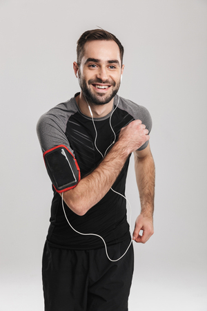 Image of a handsome young sports fitness man posing isolate over white wall background listening music with earphones running.の写真素材
