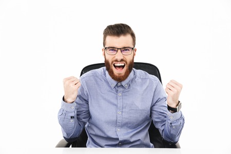 Happy screaming bearded elegant man in eyeglasses rejoices and looking at the camera while sitting...