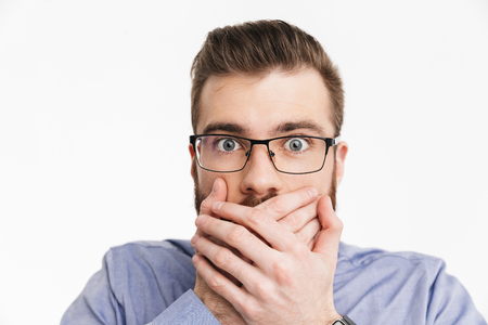 Close up image of Shocked bearded elegant man in eyeglasses covering his mouth and looking at the camera over grey backgroundの写真素材