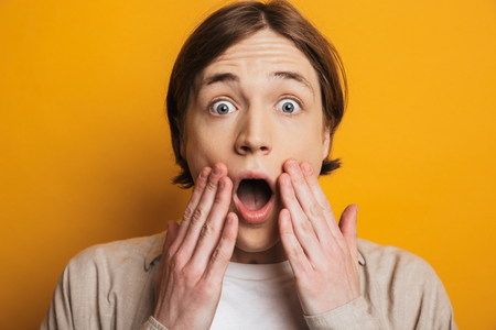 Close up of a shocked teenage boy standing isolated over yellow background, looking at cameraの写真素材