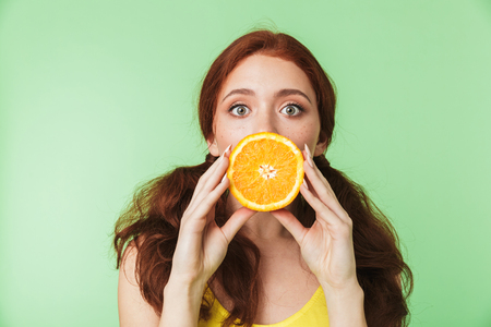 Image of a beautiful excited young redhead girl posing isolated over green wall background with citrus vitamins fruits.の写真素材