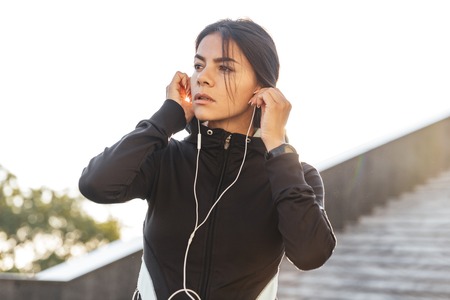 Attractive fitness woman wearing sportswear exercising outdoors, listening to music with earphonesの写真素材