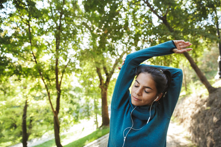 Close up of an attractive young fitness woman wearing sportswear exercising outdoors, doing...