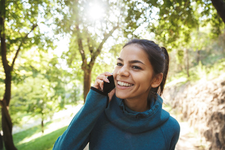 Close up of an attractive young fitness woman wearing sportswear exercising outdoors, using mobile phoneの写真素材