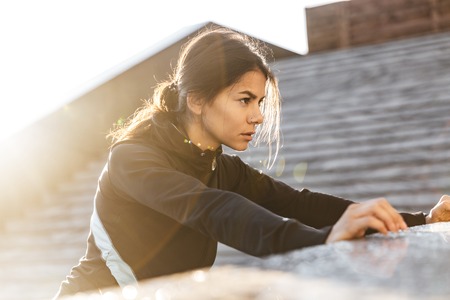 Close up of an attractive young fitness woman wearing sportswear exercising outdoors, doing...